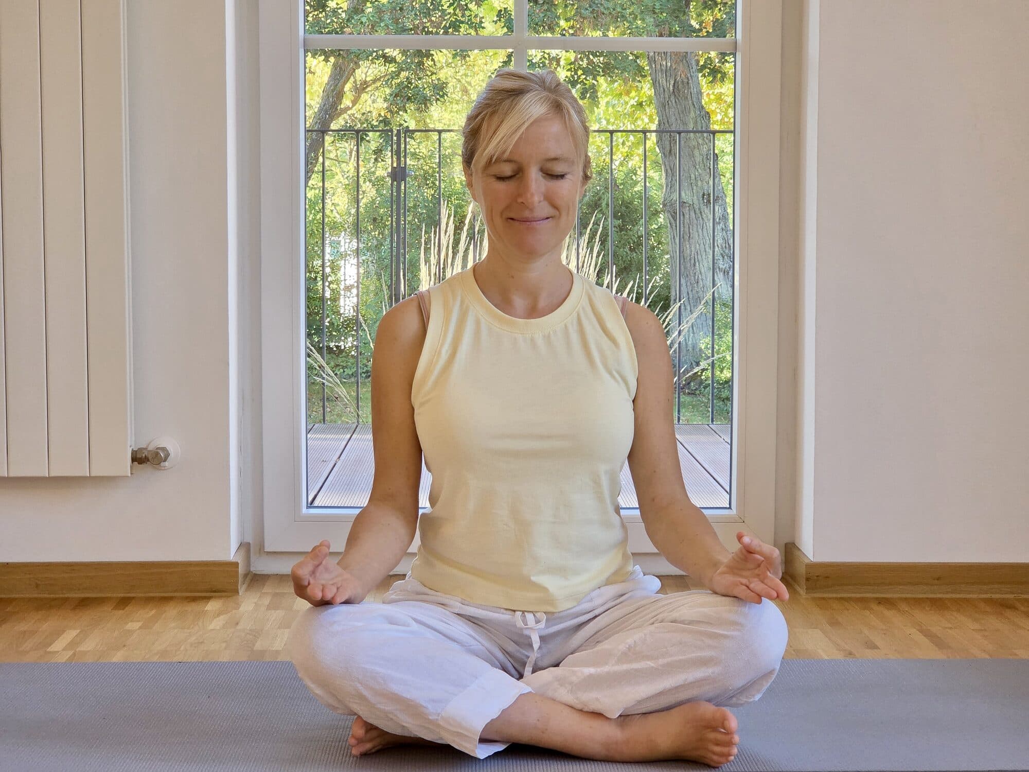 Christina Pucher meditiert im Schneidersitz auf der Yogamatte